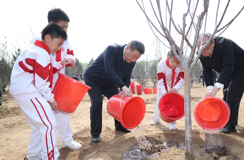 4月3日，党和国家领导人习近平、李强、赵乐际、王沪宁、蔡奇、丁薛祥、李希、韩正等来到北京市通州区潞城镇参加首都义务植树活动。这是习近平同少先队员一起给刚栽下的树苗浇水。